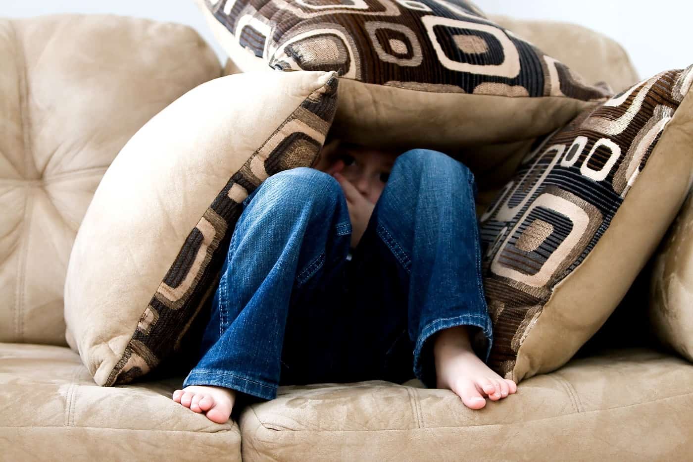 Little boy hiding under throw pillows - Family myths