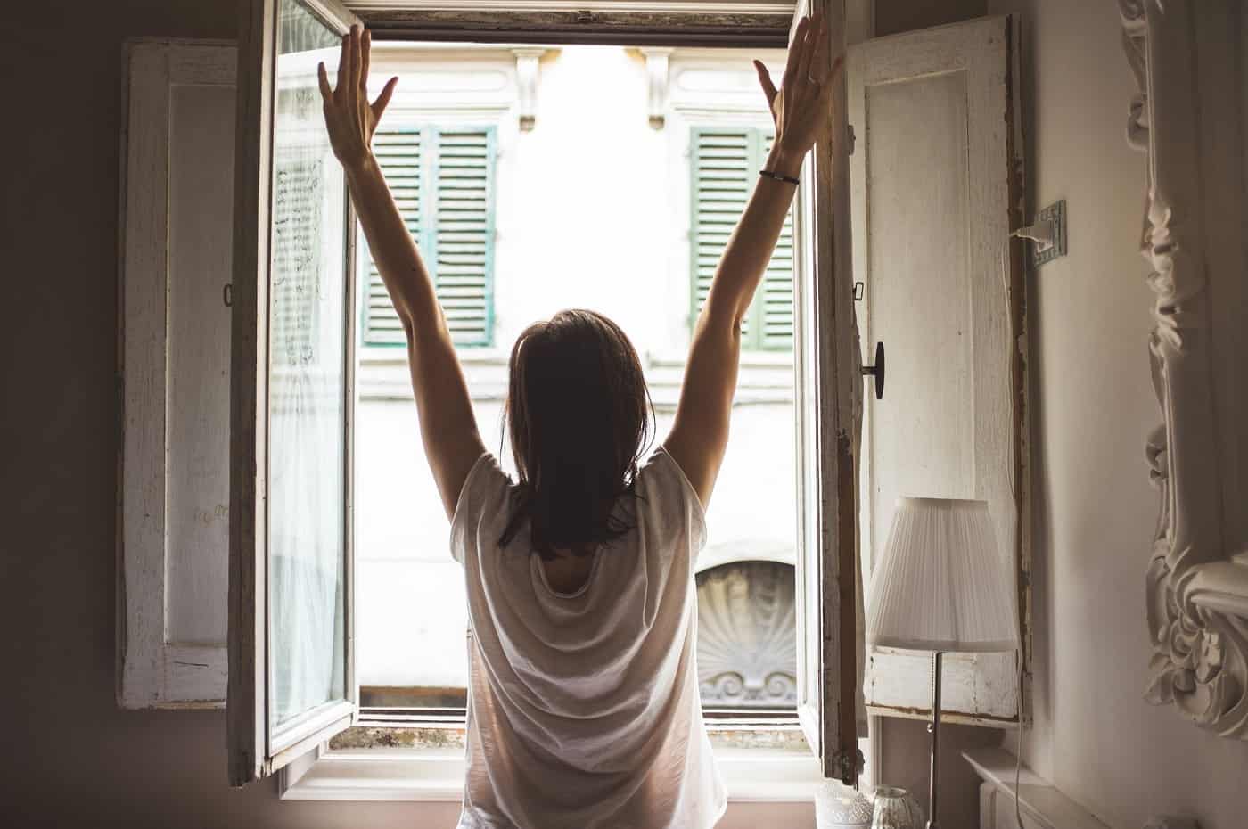 Woman stretching arms in front of window - Rise and shine