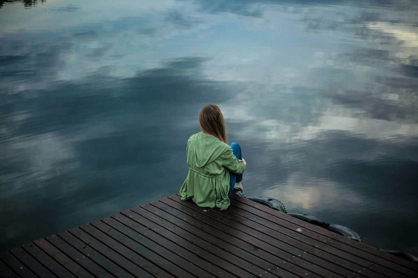 Woman sitting on dock next to lake